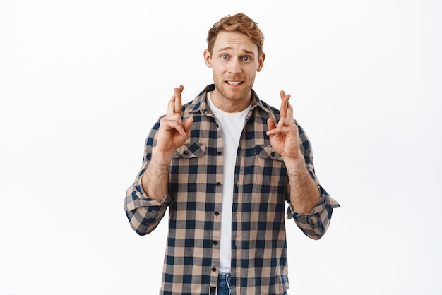 Free photo hopeful redhead adult man cross fingers and looking at camera anticipating making wish praying for dream come true waiting for miracle standing over white background