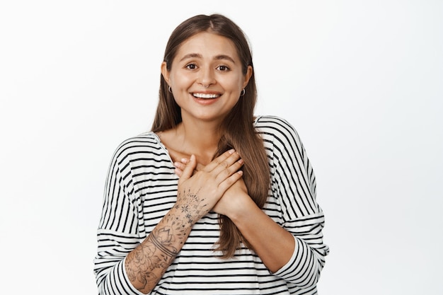 Hopeful smiling woman receiving smth, holding hands on chest and looking happy and surprised, being grateful, thank you gesture, standing on white