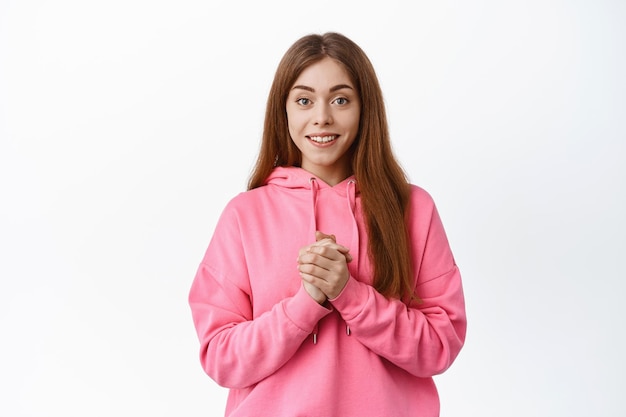 Hopeful woman clench hands and smiles at camera, anticipating something, look grateful, express gratitude, white background