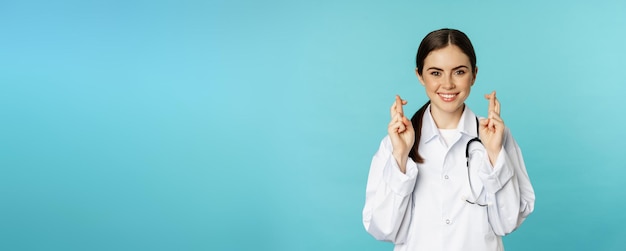 Free Photo hopeful woman doctor lab worker cross fingers and smiling praying making wish anticipating standing