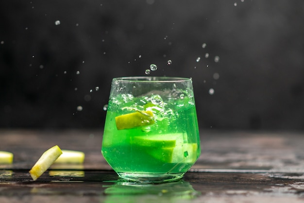 Horizontal close up view of apple juice in a glass with apple limes on dark background