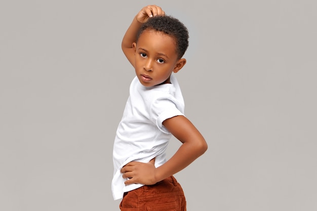 Free photo horizontal image of handsome funny eight year old dark-skinned little boy posing isolated pretending to be fashion model,