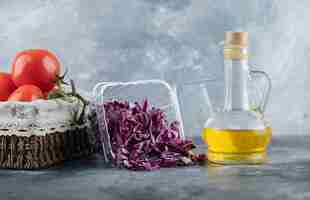 Free photo horizontal photo of fresh tomatoes with chopped cabbage and bottle of oil on grey background.