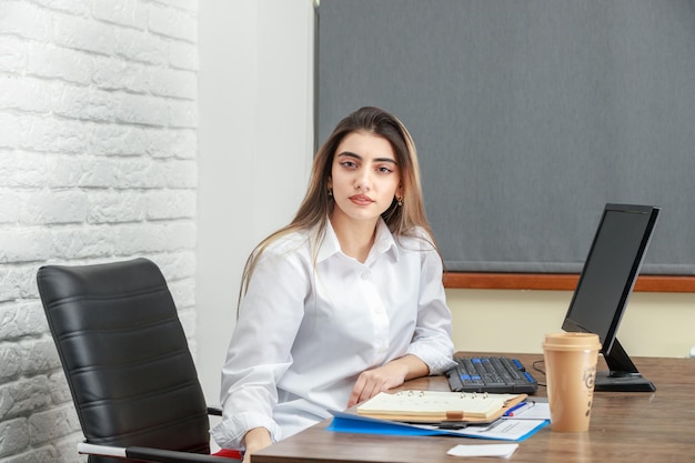 Free photo horizontal photo of young businesswoman sitting behind the desk and looking at the camera