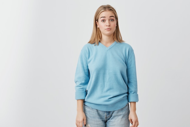 Horizontal portrait of attractive dark-eyed female dressed in blue sweater and jeans looking amazed and shocked by news she has just heard. Pretty girl posing .