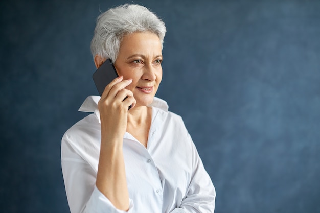 Horizontal portrait of busy middle aged Caucasian female manager in white shirt holding cell phone