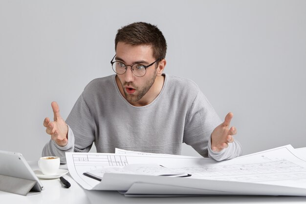 Horizontal portrait of puzzled male designer stares at screen of laptop