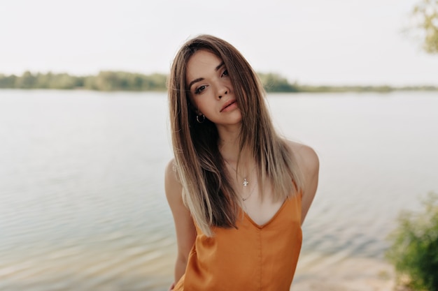 Horizontal portrait of stylish pretty model in stylish outfit posing over lake