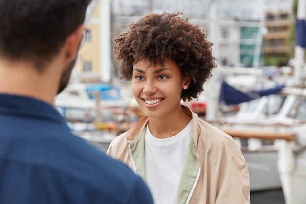 Horizontal shot of attractive Afro American girl has pleasant appearance, toothy smile