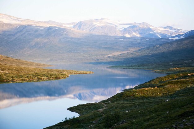 Horizontal shot of the beautiful view of the calm lake, green land and mountains