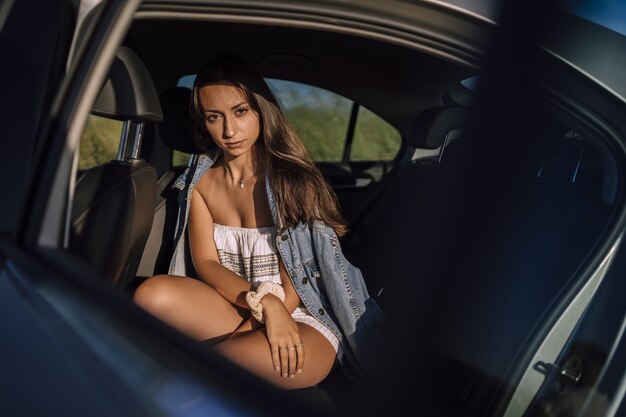 Horizontal shot of a beautiful young caucasian female posing in the back seat of a car in a field