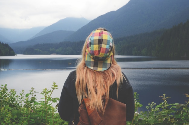 Horizontal shot of a blonde woman with a colorful cap looking at the body of water