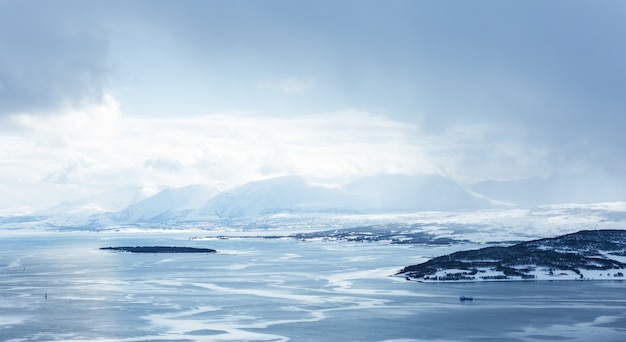 Free photo horizontal shot of a body of water covered with ice surrounded by mountains under the white clouds