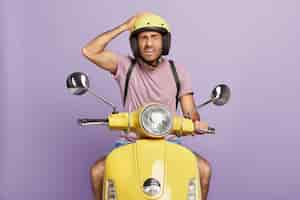 Free photo horizontal shot of displeased unshaven male driver holds hand on helmet, poses on fast motorbike, drives quickly and transports something, wears casual purple t shirt. people and transport concept