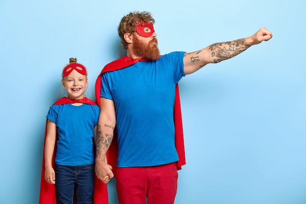 Free photo horizontal shot of feraless strong ginger father holds hand on small kid