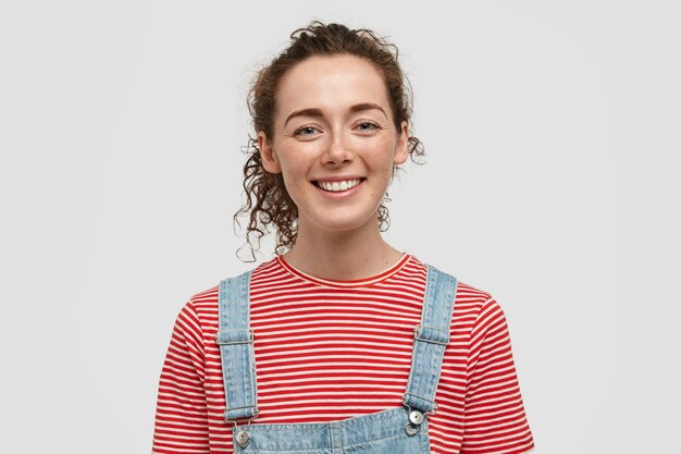 Horizontal shot of happy freckled woman adult with curly hair, pleasant smile, looks happily at camera