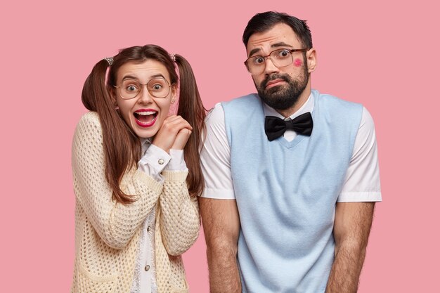 Horizontal shot of happy young European woman and man with joyful and hesitant expressions, have first date, dont know how to behave, wear old fashionable clothes, isolated over pink wall