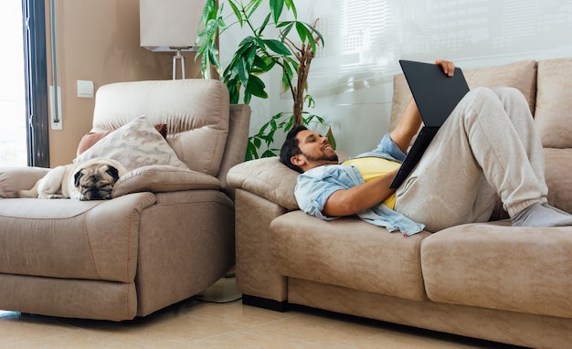 Free photo horizontal shot of a male lying on sofa at home and working with a black laptop