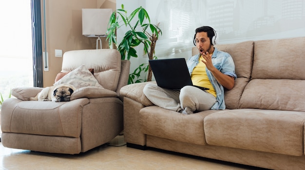 Free Photo horizontal shot of a male sitting on sofa, working with laptop and feeling shocked