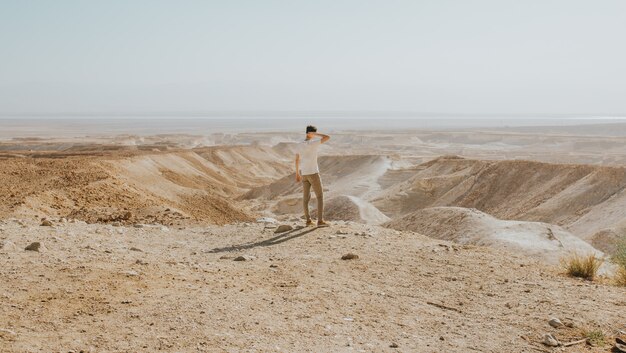 Horizontal shot of a male with a white shirt standing on the edge of a mountain enjoying the view