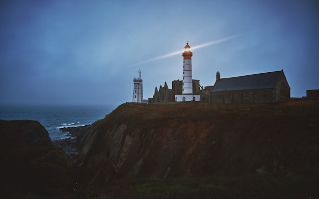 Free photo horizontal shot of a mysterious town on a cliff with a white turned-on lighthouse during dusk