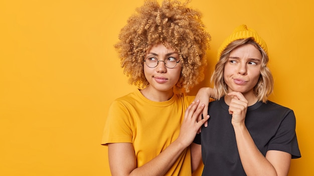 Free Photo horizontal shot of serious young women focused away and ponder on something have thoughtful expressions dressed in casual t shirts pose against yellow background copy space for your promotion