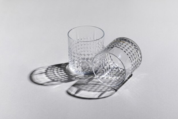 Horizontal shot of two empty old-fashioned glasses on the white surface with shadows