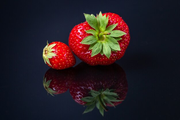 Horizontal shot of two red Croatian strawberries on a black reflecting surface