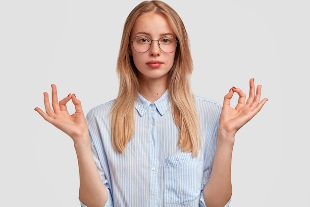 Free photo horizontal shot of young serious woman shows ok sign with fingers, being satisfied with everything, wears elegant-shirt