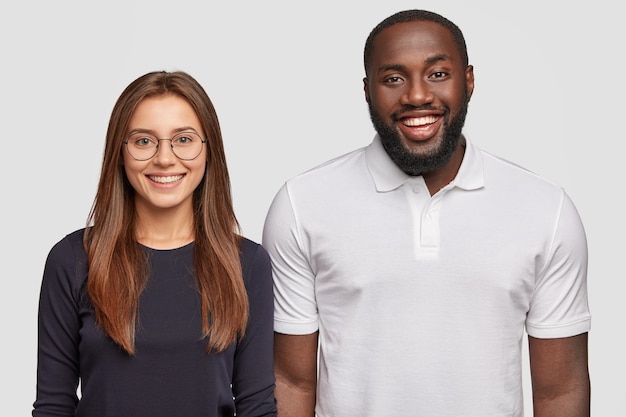 Horizontal view of cheerful dark skinned young man and European woman have positive expressions