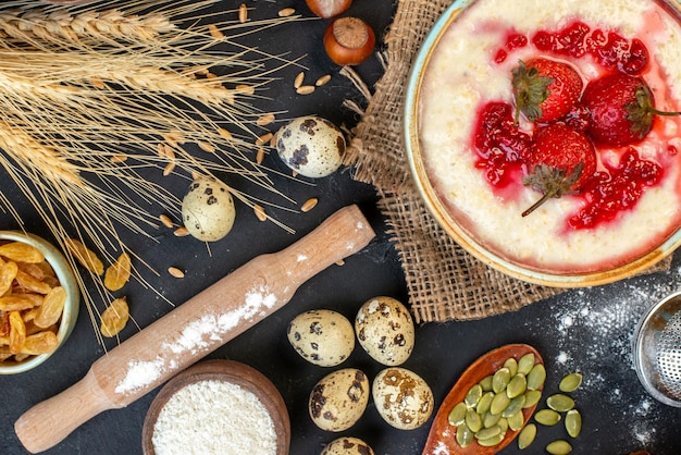 Horizontal view of delicious breakfast served with strawberries jam in a bowl and flour yellow raisins on dark color background