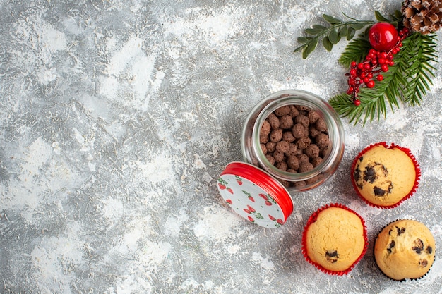 Horizontal view of delicious small cupcakes and chocolate in a glass pot and fir branches on the left side on ice surface