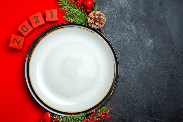 Horizontal view of New year background with dinner plate decoration accessories fir branches and numbers on a red napkin on a black table