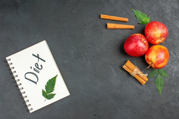 Horizontal view of spiral notebook with diet inscription and fresh apples cinnamon limes on black background