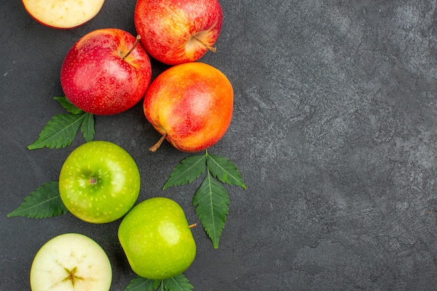 Horizontal view of whole and cut fresh red apples and leaves on the right side on black background