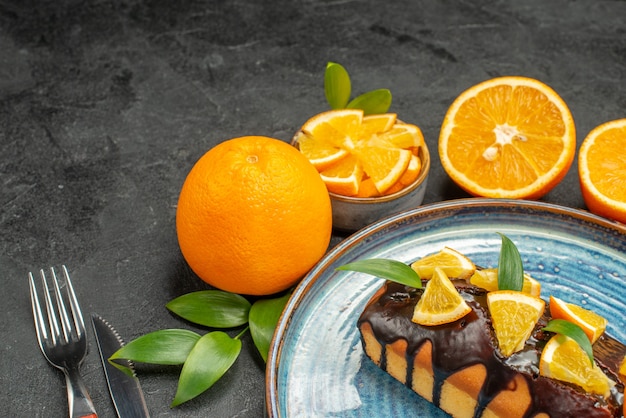 Horizontal view of yellow whole and cut lemons tasty cakes with fork and knife on dark table