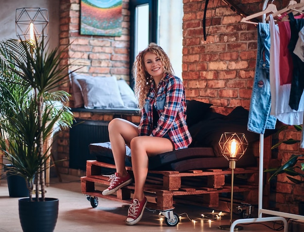 A hot blonde female dressed in denim shorts and fleece shirt posing in a studio with loft background.