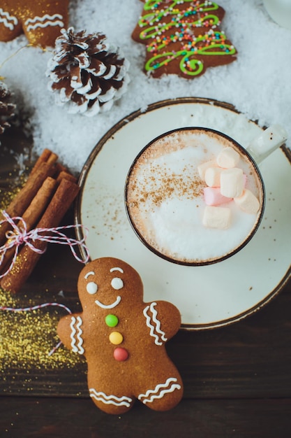 Free photo hot chocolate or cocoa beverage with cinnamon and gingerbread man cookie in snowon vintage wooden table background