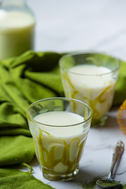 Hot green tea in a glass with cream topped with green tea, decorated with green tea powder.