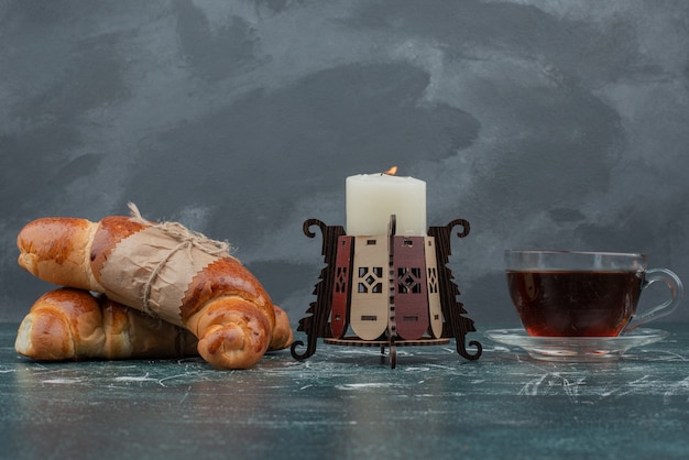 Hot tea with croissants and candle on marble table .