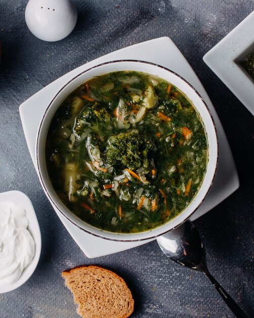 hot vegetable soup with greens boiled vegetables inside round white plate along with bread loafs eggs on grey table