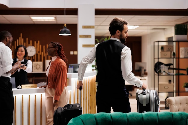 Free Photo hotel bellboy helping guests with bags, carrying luggage to room in luxury resort. young man working as concierge giving assistance to people with suitcases arriving at reception.