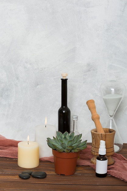 Free photo hour glass; cactus plant; lighted candle; lastone; essential oil; wooden mortar and pastel on table against wall