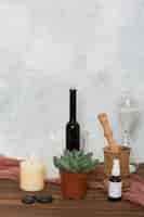 Free photo hour glass; cactus plant; lighted candle; lastone; essential oil; wooden mortar and pastel on table against wall