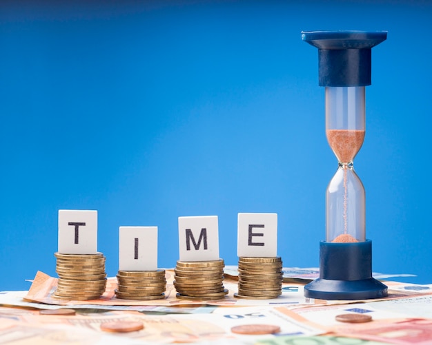 Free Photo hourglass next to pile of coins assortment