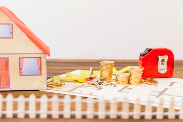 House besides measure tape, stacked coins and key on blueprint