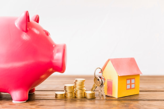 House with key and stacked coins besides piggybank