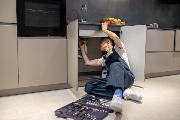 Free photo household repair middle aged man inspecting pipe touching hand under sink in stylish modern kitchen