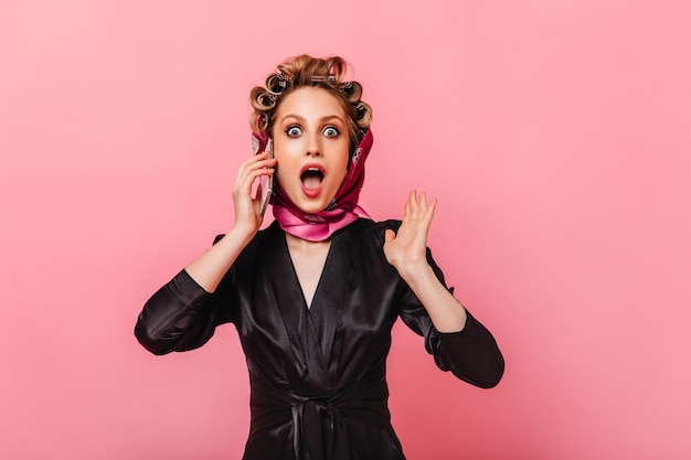 Free photo housewife in dressing gown and scarf looks at front in amazement and talks on phone