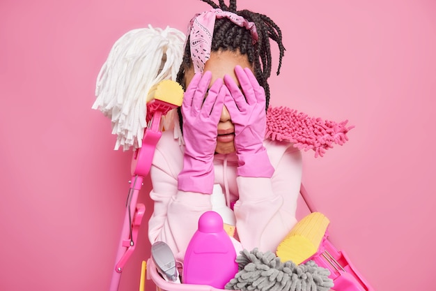 Free photo housewife tired of cleaning up all house cries and cons face with hands in rubber gloves surrounded by cleaning supplies expresses negative emotions isolated on pink